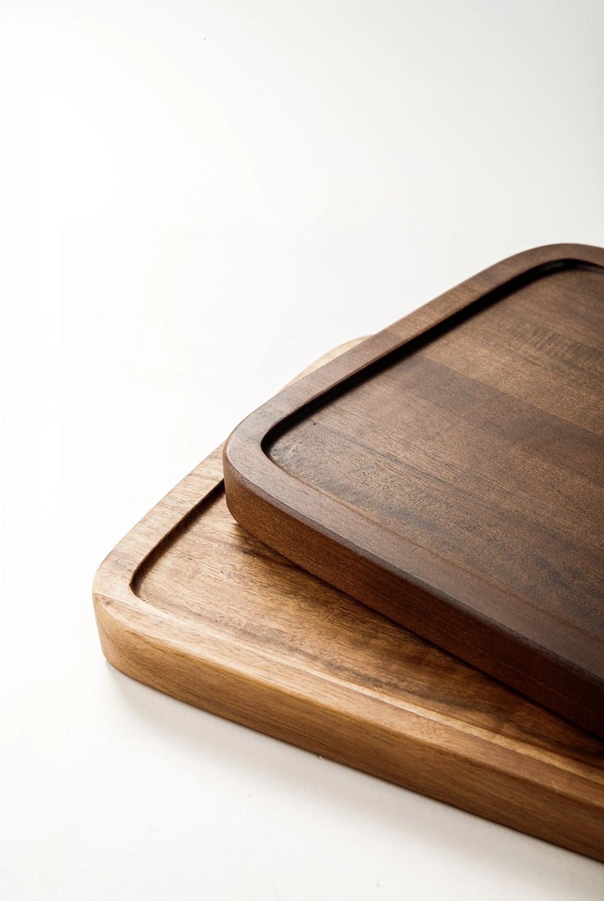 Stacked acacia and walnut wood cutting boards on a white surface
