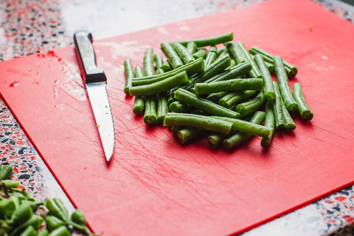 Red plastic cutting board with chopped green beans and knife